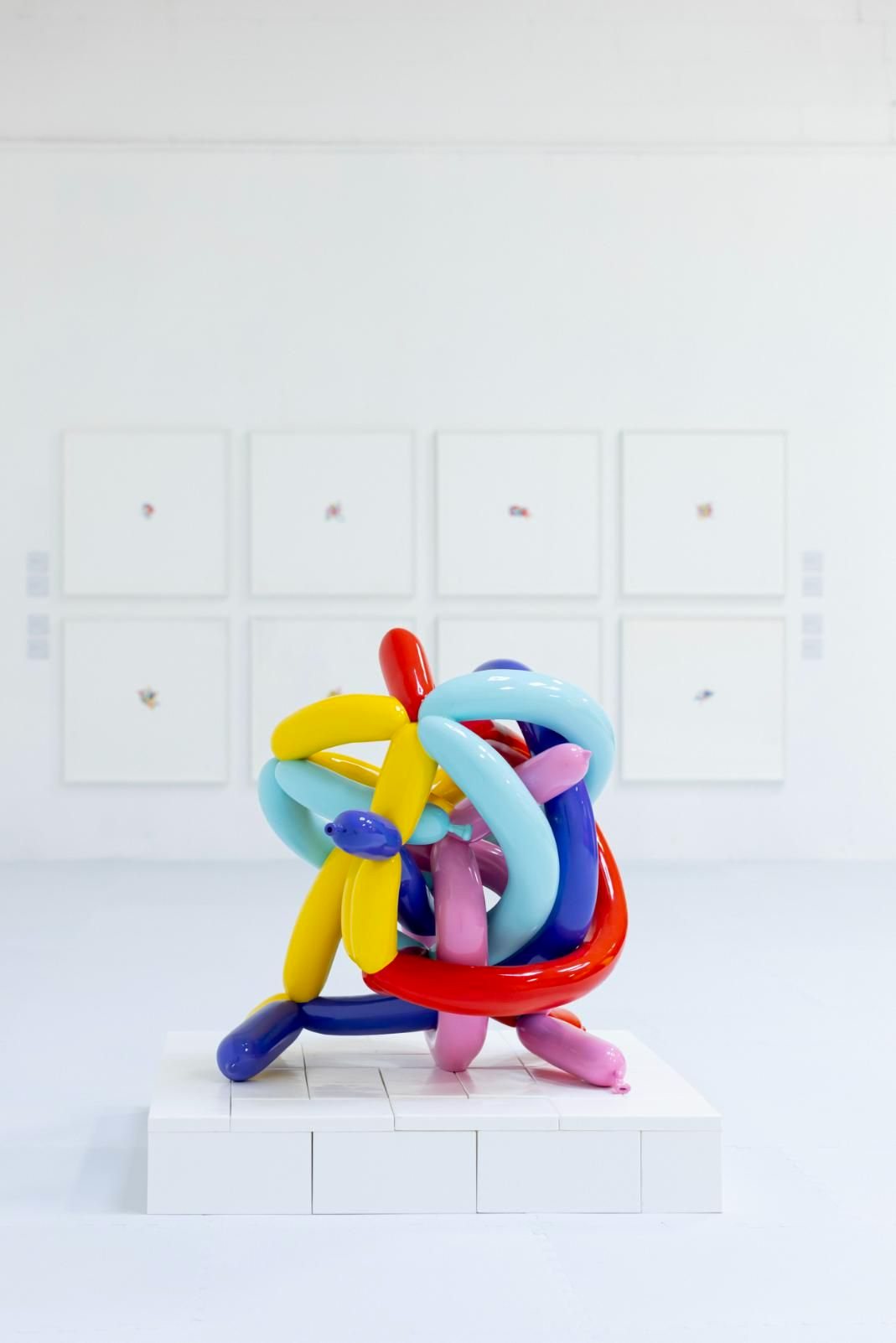 A glossy tangle of multicoloured balloon forms on a white plinth