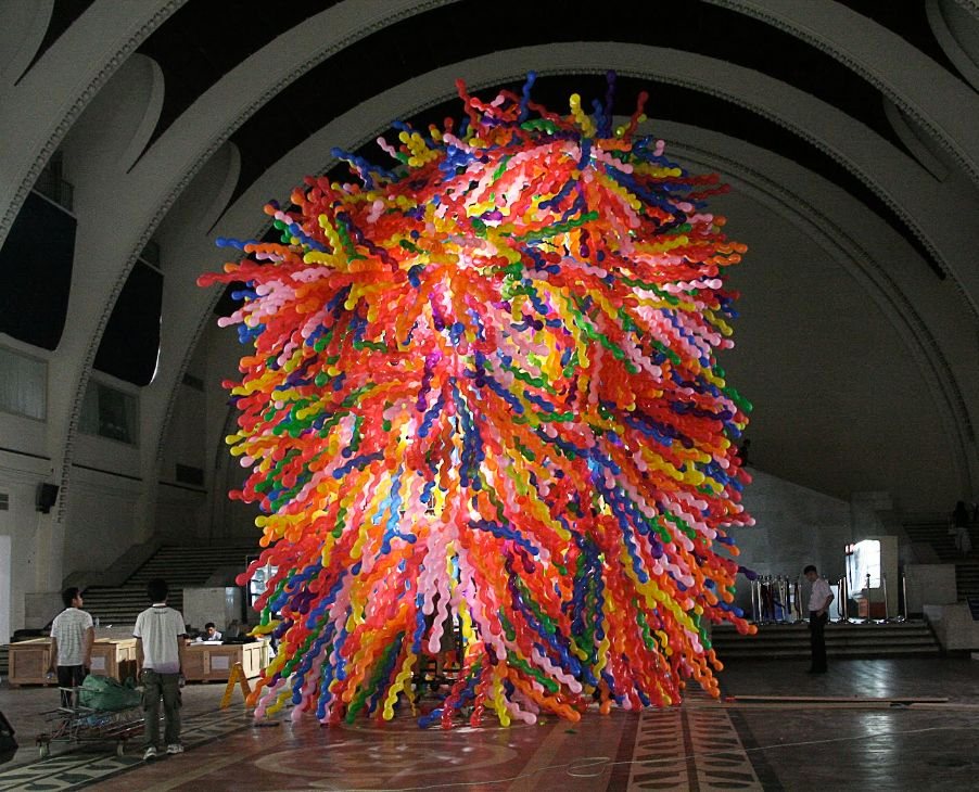 A giant burst of multicoloured balloons in a vaulted hall