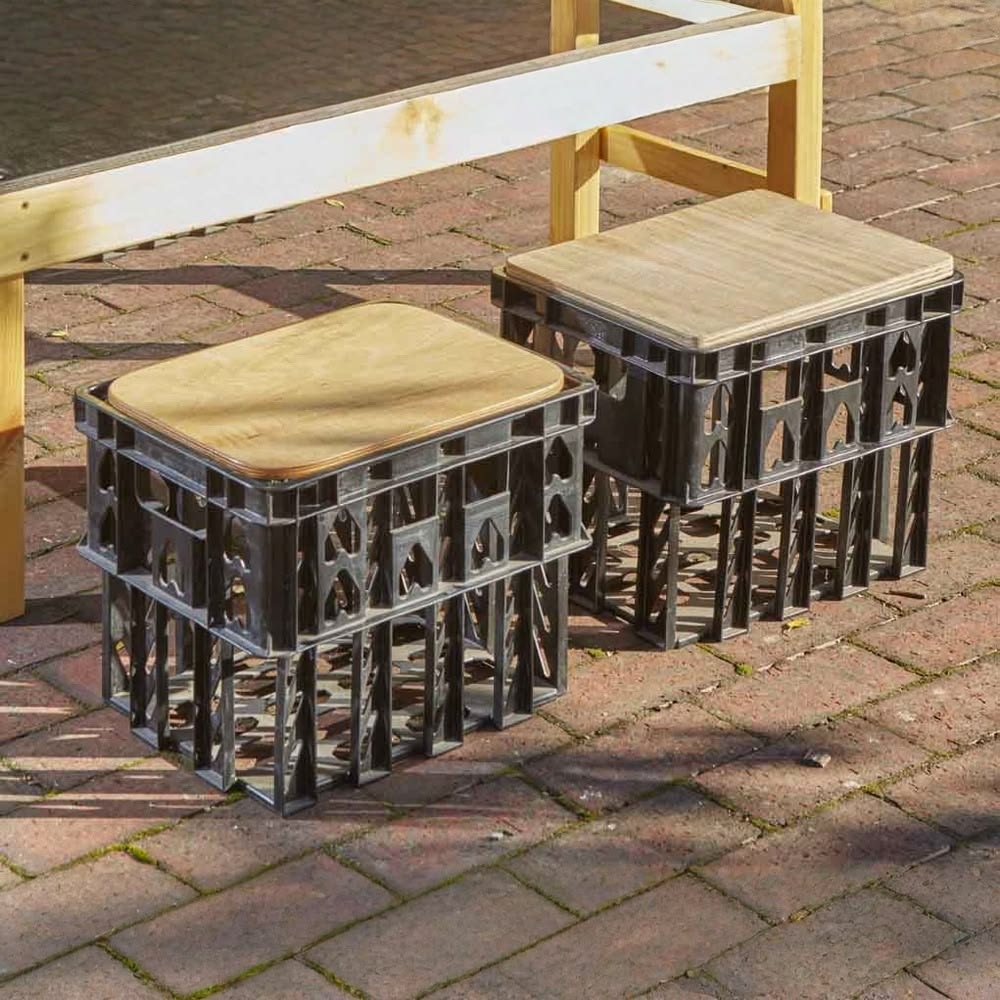 Two black crates topped with wooden seats on a brick yard