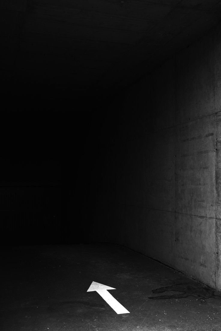 A dark corridor with a single white arrow painted on the floor
