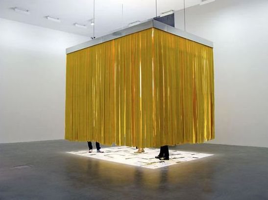A yellow curtained cube suspended from the ceiling over a lit floor