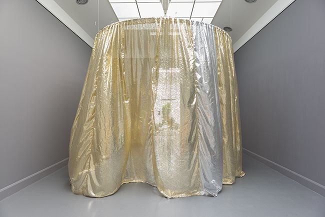A form draped in gold fabric standing in a white gallery