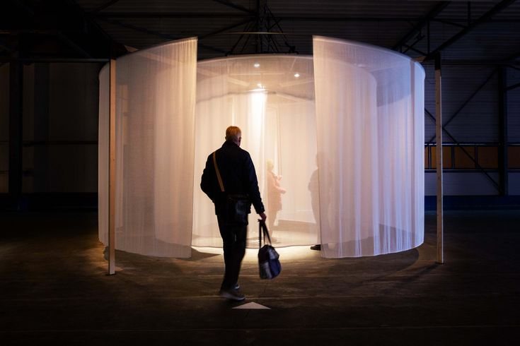 A figure walking into a tall drum of sheer white curtain
